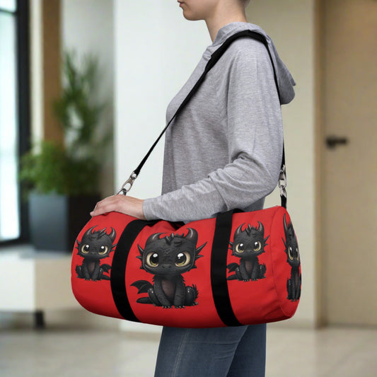 a red duffel bag with black straps and shoulder strap and black betty baby dragon is on each side 3 times and on each end