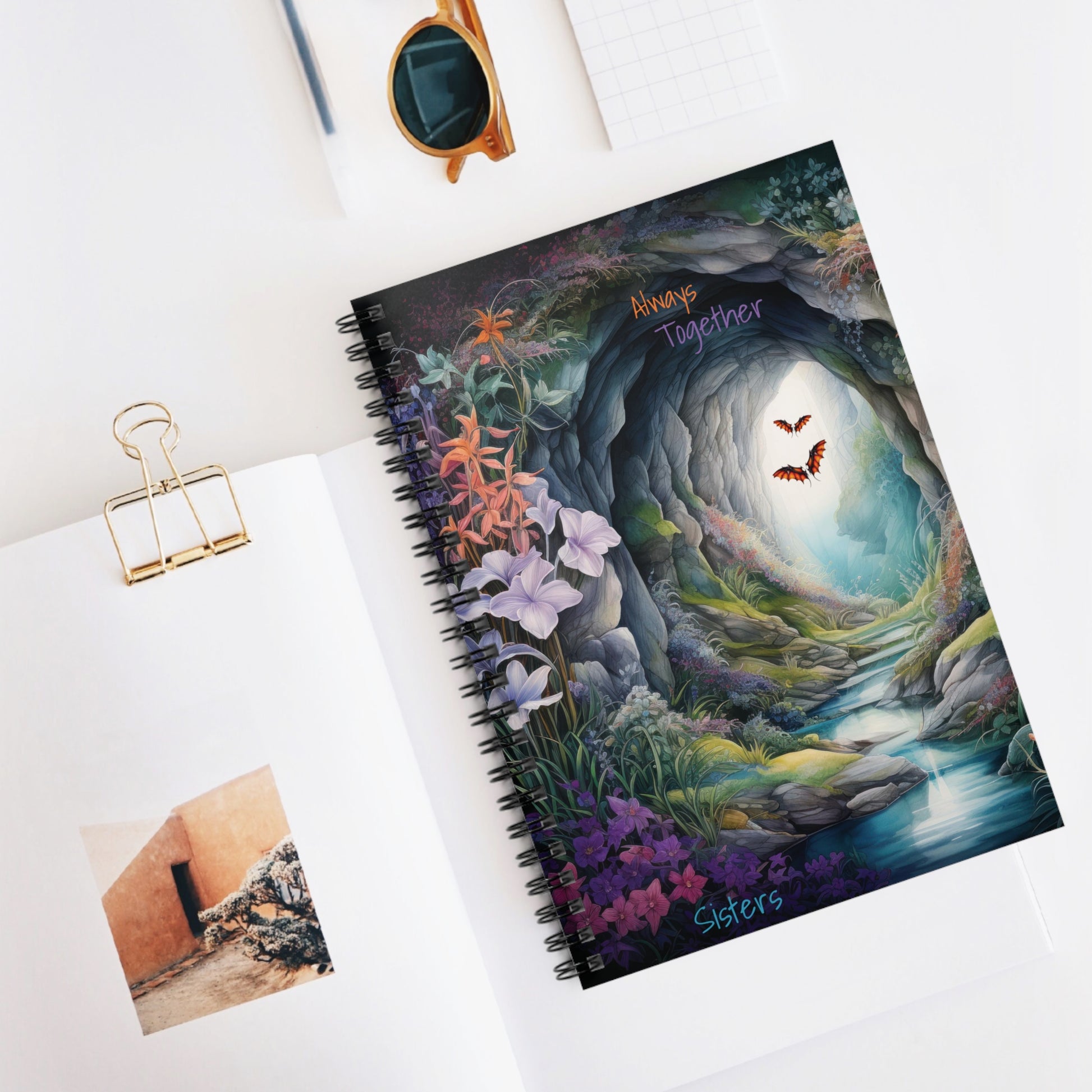 Always Together Sisters is the text on a front cover design on a spiral notebook - a blue cave beacons to you with a stream leading in flowers surround the cave entrance the cave leads into another realm?